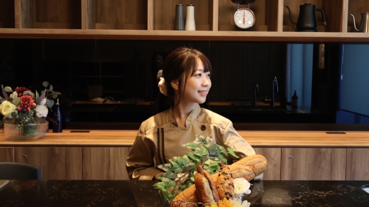 コックコート姿でパンかごの後ろに立つパン職人むぎ